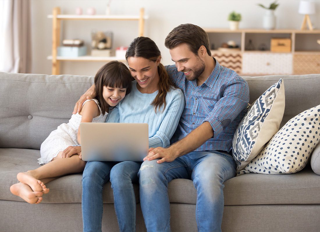 About Our Agency - Married Diverse Couple and Little Preschool Daughter Sitting on Couch Using Computer