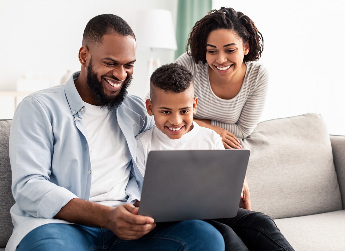 Insurance Solutions - A Young Happy Family Looking Down at Their Laptop While Smiling